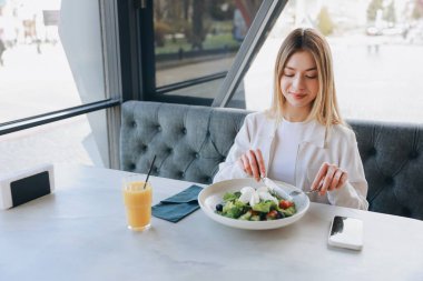 Mozarella peynirli taze salata yiyen ve cafe masasında meyve suyu içen dengeli diyet ve sağlıklı yaşam tarzı olan genç bir kadın.