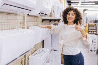 Müşteri, satın alma kararından memnun bir şekilde bir mağazada klima seçerken başparmak kaldırıyor.