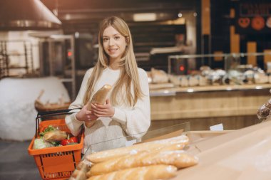 Müşteri bir süpermarketten ekmek seçiyor, elinde alışveriş sepeti tutuyor.