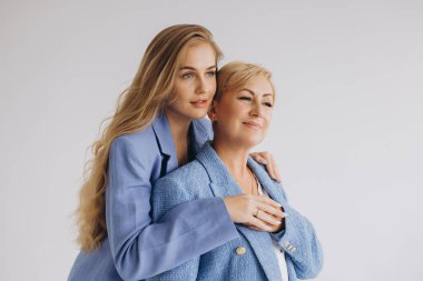 Daughter hugging her mother, both wearing elegant blue suits, sharing a tender moment of love and complicity