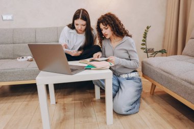 Two students studying together at home, using a laptop and traditional books while preparing for their upcoming exam in a cozy living room