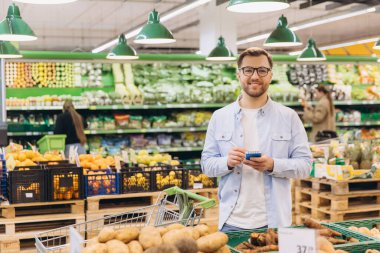 Man writing shopping list on notepad, choosing fresh vegetables and fruits in grocery store
