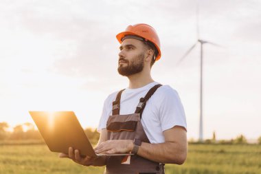 Engineer using a laptop, working in a wind turbine power plant at sunset, renewable energy concept