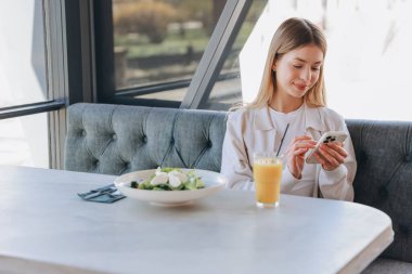 Businesswoman enjoying a nutritious lunch while browsing her smartphone in a stylish restaurant, embracing a modern lifestyle and relaxation