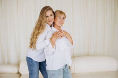 Daughter hugging her mother from behind, expressing love and connection in a bright interior setting