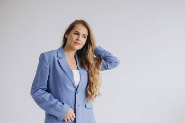 Confident young businesswoman adjusting her hair, wearing a stylish blue suit against a white background, exuding professionalism and poise