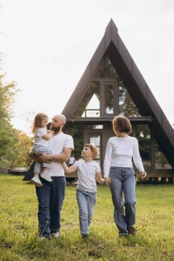 Happy family enjoying a walk on the grass in front of their contemporary a frame house, embracing the joys of togetherness and modern living