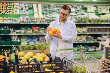Customer selecting fresh oranges while shopping in a grocery store, focusing on nutritious food options for a healthy lifestyle