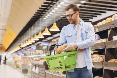 Customer wearing protective gloves choosing bread in bakery section at grocery store