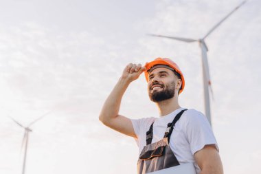 Smiling engineer adjusting his helmet while working on a wind turbine, contributing to the advancement of renewable energy solutions