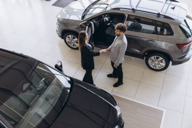Top view of a car salesperson shaking hands with a customer in a dealership after closing a deal for a new vehicle