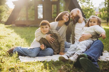 Smiling family with two children relaxing on blanket in backyard, enjoying quality time together on sunny day