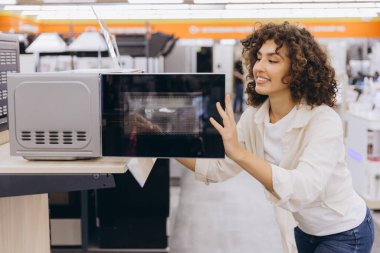 Smiling woman checking microwave oven, shopping for kitchen appliances in home appliance store