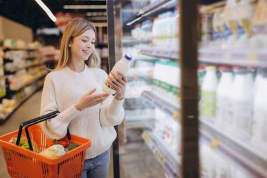 Müşteri marketin buzdolabı reyonunda alışveriş yaparken süt şişesi etiketi okuyor