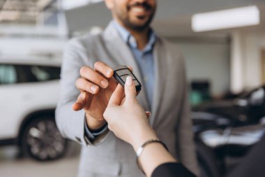 Car salesman handing over the keys of a new car to a customer in a car dealership, closing a successful deal