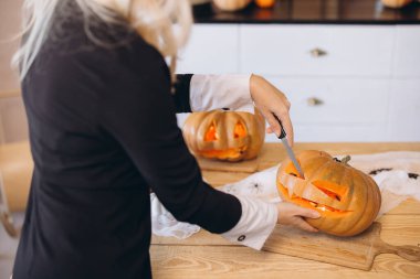 Woman carving a spooky face on a pumpkin, preparing for a festive Halloween celebration in a cozy kitchen filled with autumn vibes