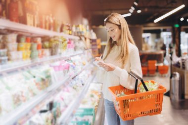 Customer writing on notepad while holding a shopping basket and choosing groceries in a supermarket