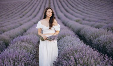 Model wearing a flowing white dress, holding a vibrant bouquet of lavender flowers while surrounded by a picturesque lavender field
