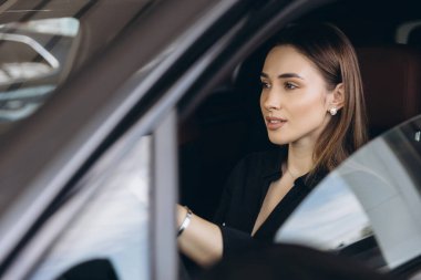 Businesswoman sitting in a new car and trying it at the dealership