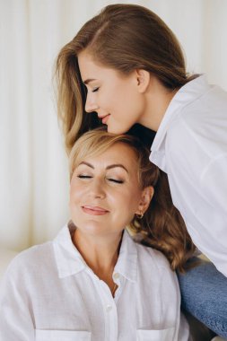 Daughter gently resting her head on her mother's, both with closed eyes and serene expressions, highlighting the strong bond between them