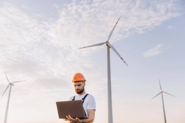 Engineer is working with a laptop in a wind turbine power plant, checking the energy production