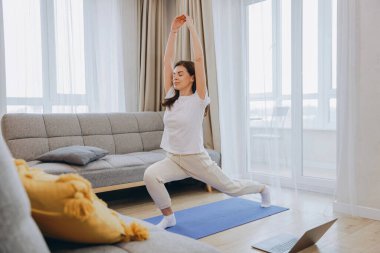 Woman practicing yoga at home following online class on laptop, promoting wellness and healthy lifestyle