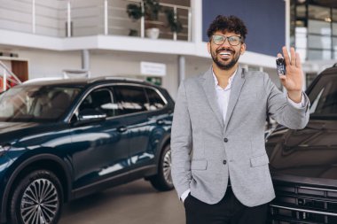 Man in dealership holding car keys, showcasing new vehicles