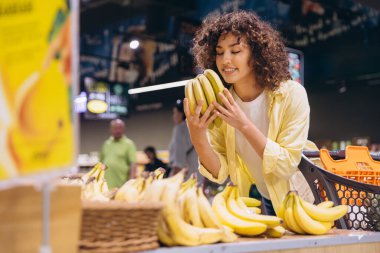Customer enjoying the aroma of fresh bananas while shopping for groceries in a vibrant supermarket, selecting quality produce for a healthy diet