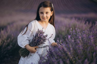 Girl wearing a white dress holding a bouquet of lavender in a lavender field, enjoying the scent and the beautiful purple landscape