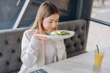 Happy customer enjoying healthy meal in a restaurant, smelling fresh salad before eating it, orange juice on the table