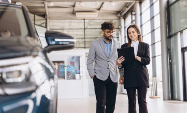 Salesperson engaging with customer while showcasing a new car at a modern dealership, discussing options and financing details for purchase