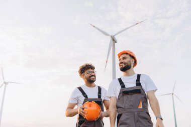 Two engineers discussing near wind turbines, enjoying their successful work in sustainable energy generation