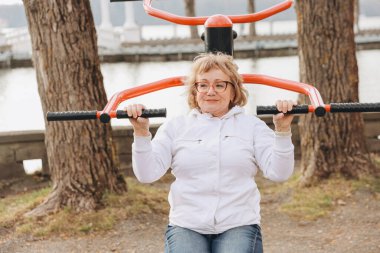 Elderly woman exercising outdoors using public gym equipment, promoting healthy aging and active lifestyle