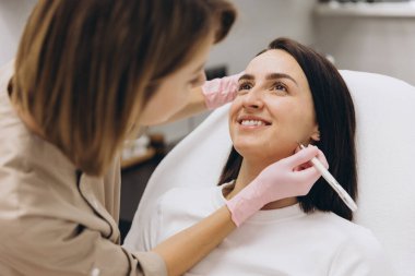 Cosmetologist drawing marks on a smiling woman's face before botox injections in a medical office