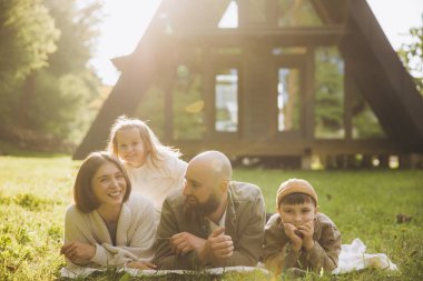 Family lying on blanket in the garden of their modern a frame house, enjoying a moment of relaxation together