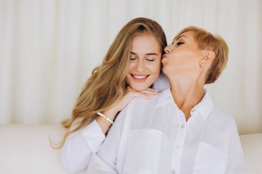 Mother expressing love and affection by kissing her daughter on the cheek, showcasing a tender moment of family bonding
