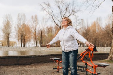 Elderly woman enjoying a workout session in an outdoor gym, promoting healthy aging and active lifestyle
