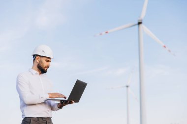 Engineer using laptop, controlling wind turbines in a power plant for sustainable energy production