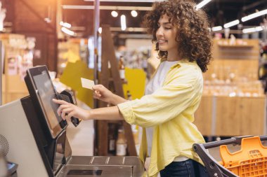 Customer using credit card to pay for groceries at a self service checkout in a modern supermarket