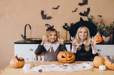 Mother and daughter creating spooky faces while joyfully carving pumpkins together, preparing for a festive Halloween celebration