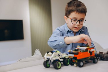 Child wearing glasses playing with colorful construction toys, developing fine motor skills and creativity in a comfortable home environment