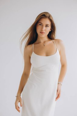 Studio portrait of a young woman wearing a white dress, her hair flowing gently as she poses against a white backdrop
