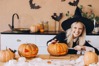Happy witch joyfully carving a spooky face on a pumpkin, embracing the festive spirit of Halloween celebrations in the kitchen