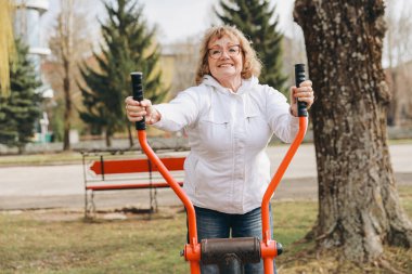 Elderly woman working out on a public elliptical trainer, promoting healthy aging and active lifestyle