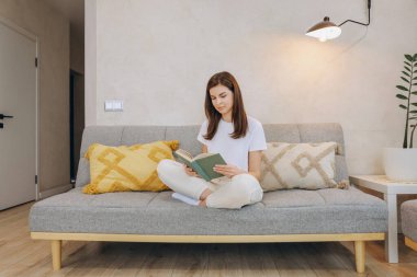 Young woman enjoying a relaxing moment reading a book while sitting comfortably on her sofa at home