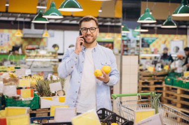 Customer holding lemons and making a phone call while shopping for groceries in a supermarket
