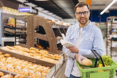 Customer wearing gloves choosing bread from bakery shelf reading recipe book in grocery store