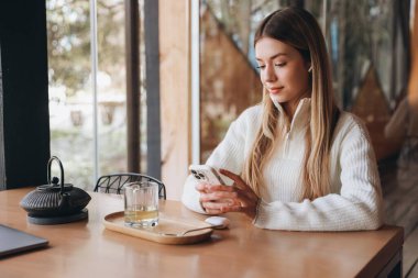 Freelancer working remotely from a cafe, enjoying a cup of tea and using mobile phone and earphones