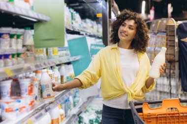 Customer selecting fresh milk in grocery store, holding bottle and checking labels on refrigerated shelf, making healthy choices for balanced diet