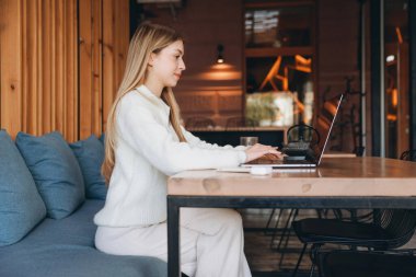 Freelancer immersed in work, typing on a laptop while enjoying a cozy atmosphere in a charming cafe, balancing productivity and comfort